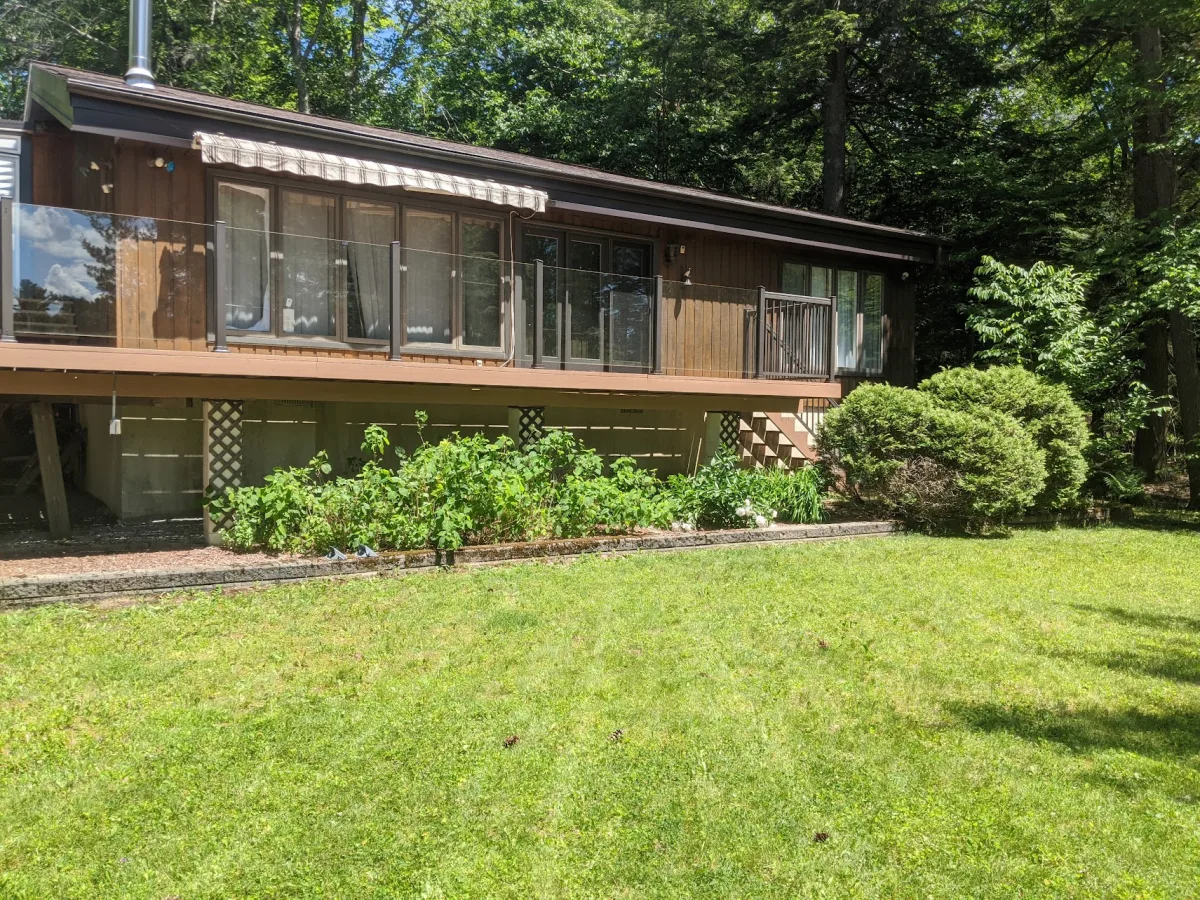 A deck with glass railings above a garden beside a wooded home