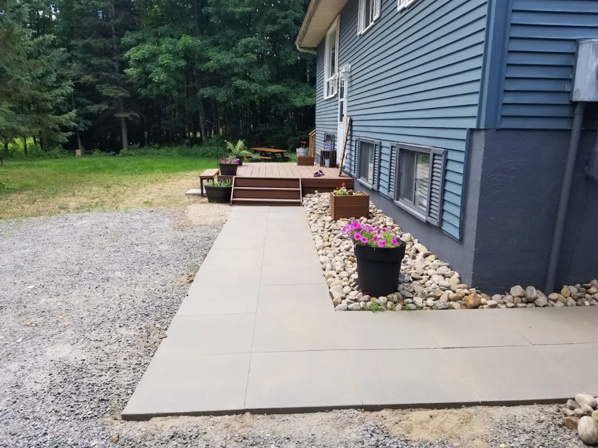 A paved walkway beside a blue home, with stone borders and flower planters
